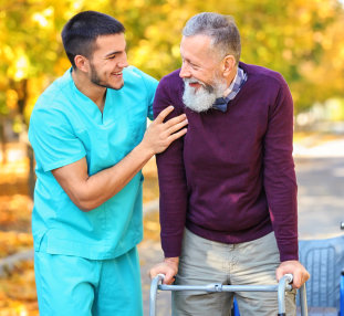 male caregiver helping senior man walk with his walker